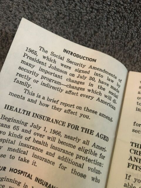 A close-up photograph of an open book with slightly yellowed pages. The text discusses the Social Security Amendments of 1965, signed into law by President Lyndon B. Johnson on July 30, 1965. The introduction mentions that these amendments brought significant changes to the Social Security program, affecting many Americans. The section titled "Health Insurance for the Aged" explains that starting July 1, 1966, nearly all Americans 65 and older would become eligible for two kinds of health insurance protection, marking the introduction of Medicare. The book appears to be an official government-issued pamphlet or informational booklet. The background is a soft, textured gray fabric, possibly a towel or carpet.